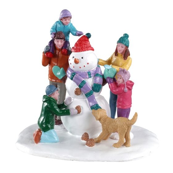 Scène de village de Noël - Famille construisant un bonhomme de neige