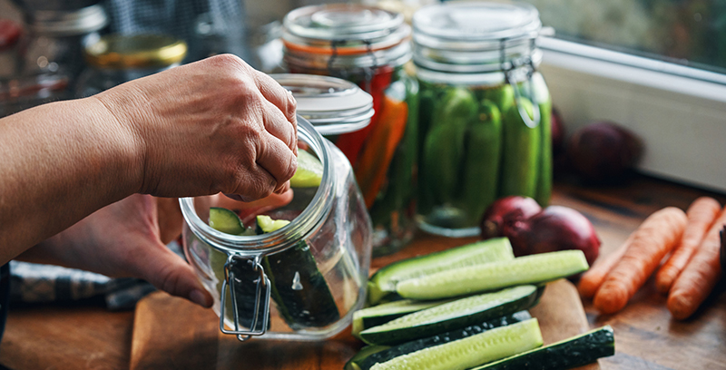 Person placing sliced cucumbers inside a glass jar