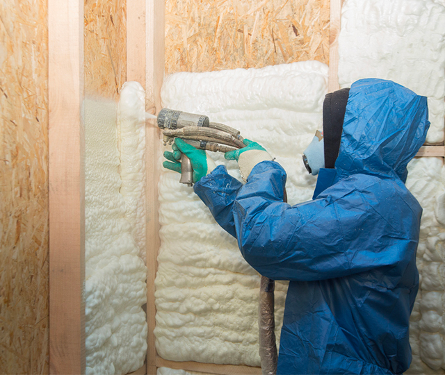 Ouvrier pulv&eacute;risant de la mousse isolante &agrave; l'int&eacute;rieur de la structure d'un mur