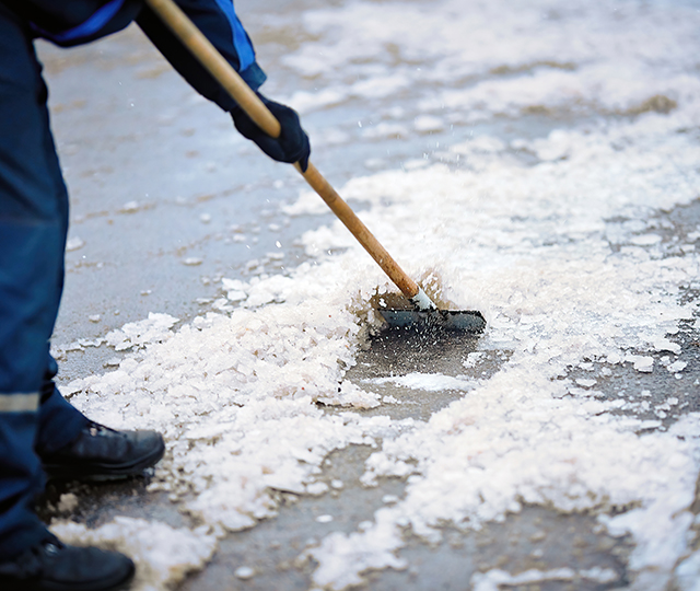 Person using an ice scraper to remove ice and snow from an outdoor surface.