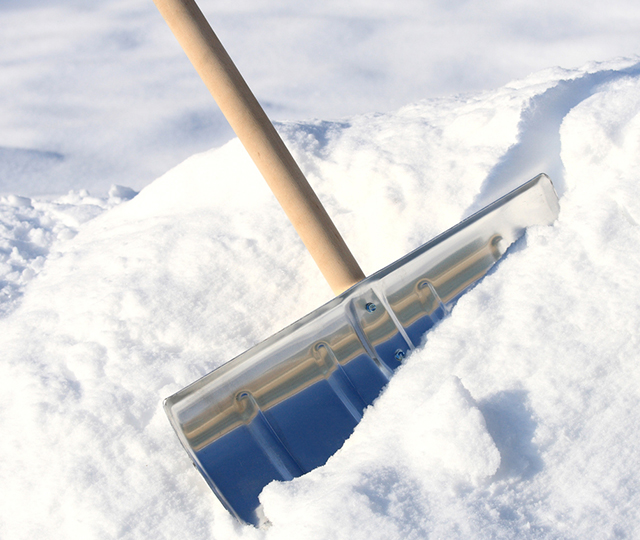 Aluminum snow pusher with wooden handle clearing a snow-covered surface.