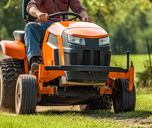 Personne conduisant un tracteur-tondeuse sur une grande pelouse résidentielle. Le visuel illustre l'entretien du gazon à l'aide d'une tondeuse autoportée pour une coupe efficace des grands terrains.