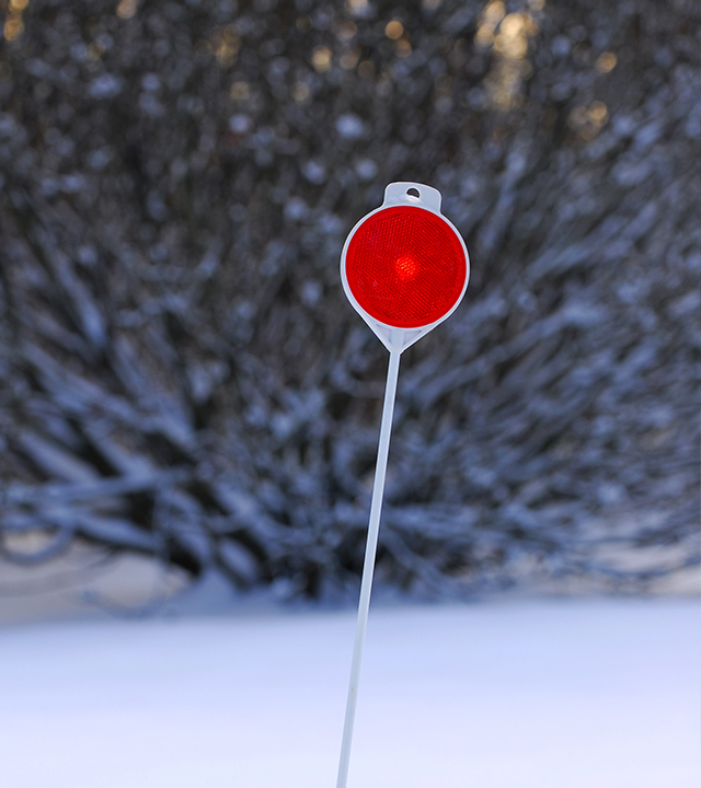 A street marker with a reflector planted in the snow.