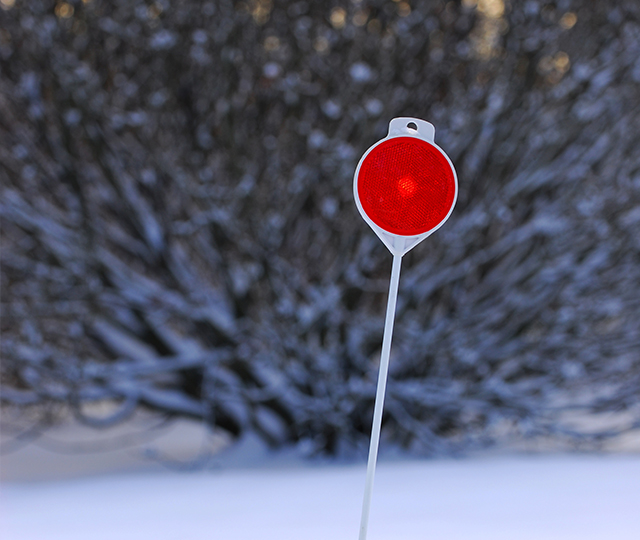 A street marker with a reflector planted in the snow.