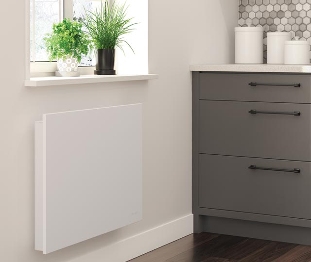 Convector heater installed on a bathroom wall, placed under a window with plants and next to a sink.