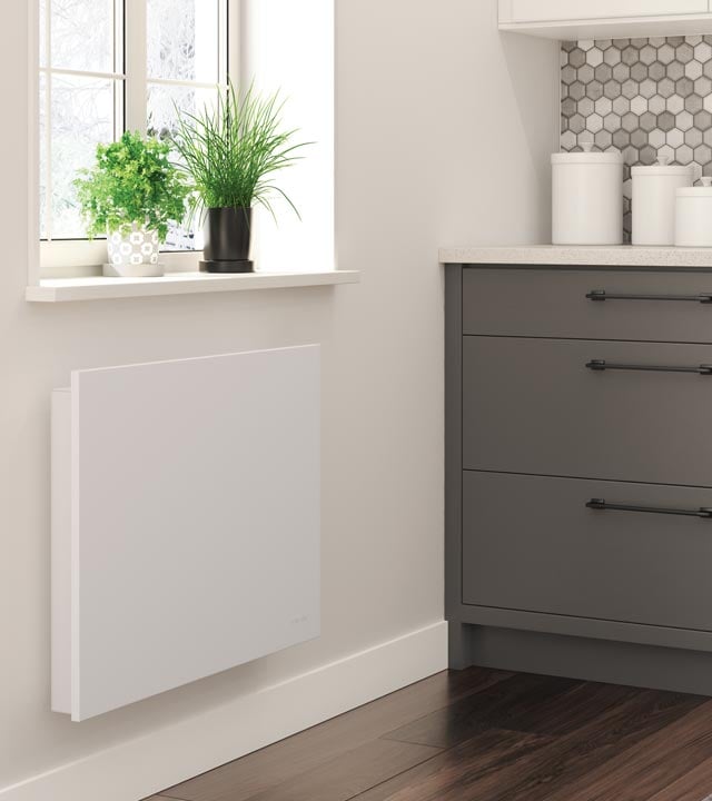 Convector heater installed on a bathroom wall, placed under a window with plants and next to a sink.