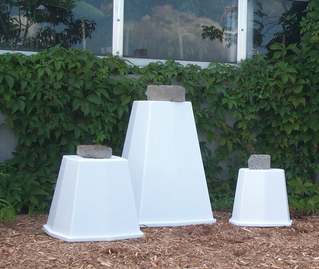 Trois cônes en polystyrène protégeant chacun une plante, avec une brique de béton posée sur le dessus.