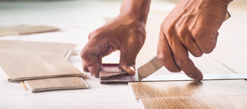 Très gros plan sur un homme en train de découper une planche de plancher SPC avec un exacto et une équerre.