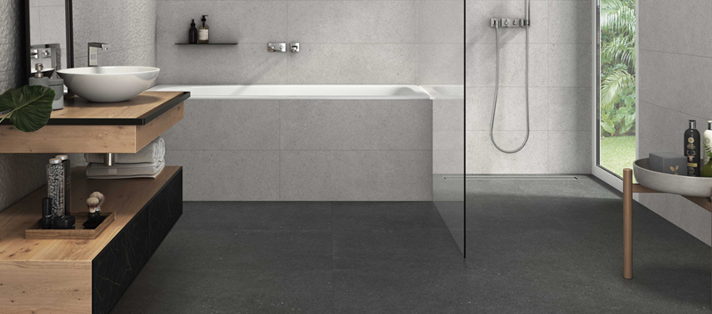 Salle de bain moderne avec plancher en c&eacute;ramique fonc&eacute;e, baignoire encastr&eacute;e, douche vitr&eacute;e et meuble-lavabo en bois naturel.