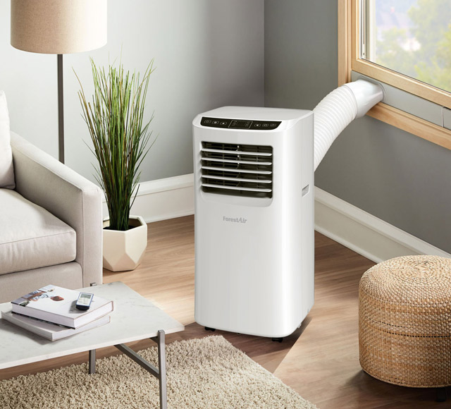 Climatiseur portatif blanc avec tuyau d&rsquo;&eacute;vacuation raccord&eacute; &agrave; une fen&ecirc;tre, plac&eacute; dans un salon lumineux.