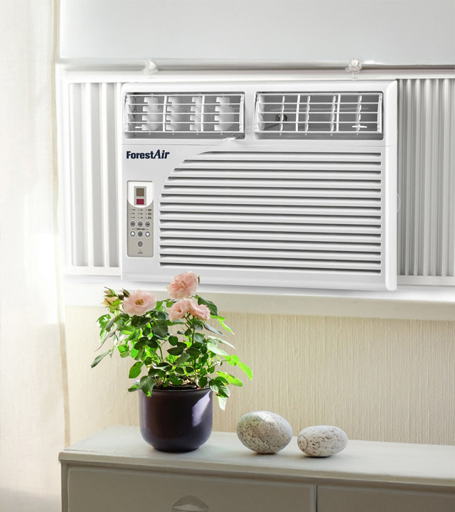 Climatiseur de fen&ecirc;tre blanc install&eacute; dans une pi&egrave;ce lumineuse, avec panneau de commande lat&eacute;ral et plante d&eacute;corative au premier plan.