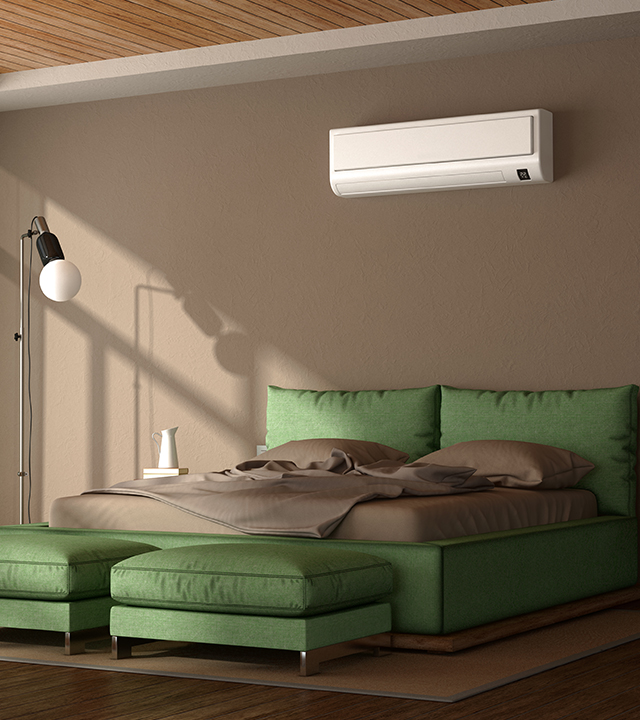 Climatiseur mural de type mini-split install&eacute; au-dessus d&rsquo;un lit dans une chambre moderne aux tons verts et bois.