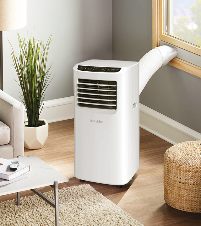 Climatiseur portatif blanc avec tuyau d&rsquo;&eacute;vacuation raccord&eacute; &agrave; une fen&ecirc;tre, plac&eacute; dans un salon lumineux.