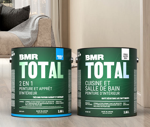 Gallons de peinture de marque BMR déposés sur le plancher d'un salon où l'on voit un canapé beige en arrière-plan.