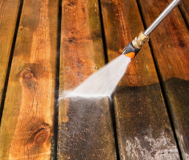 Nettoyeur haute pression pulvérisant une terrasse en bois pour nettoyer la surface avant l’application de la teinture.