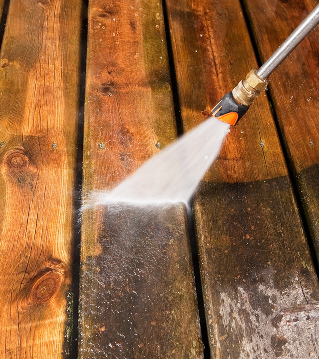 Nettoyeur haute pression pulvérisant une terrasse en bois pour nettoyer la surface avant l’application de la teinture.