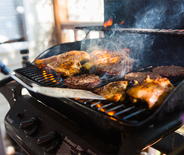 Barbecue au gaz en fonctionnement avec poulet et steaks en cuisson sur la grille.