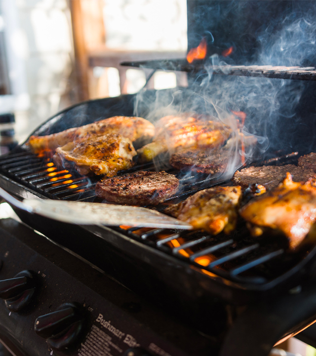 Barbecue au gaz en fonctionnement avec poulet et steaks en cuisson sur la grille.