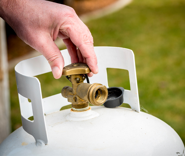 Main ouvrant la valve d&rsquo;une bonbonne de propane pour alimentation d&rsquo;un barbecue.