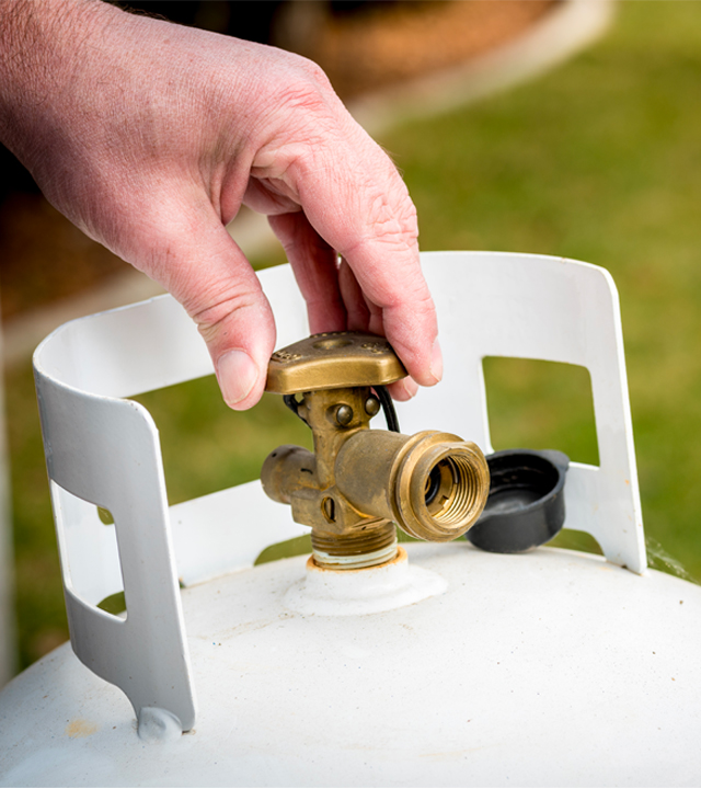 Main ouvrant la valve d&rsquo;une bonbonne de propane pour alimentation d&rsquo;un barbecue.