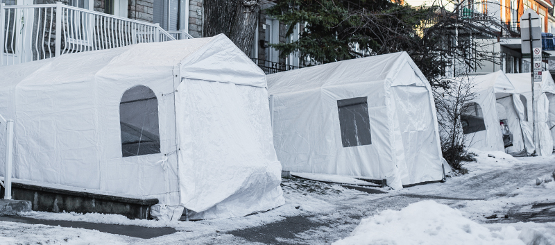 White temporary car shelters installed in front of homes along a snow-covered residential street in winter.