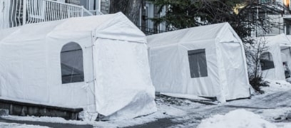 White temporary car shelters installed in front of homes along a snow-covered residential street in winter.