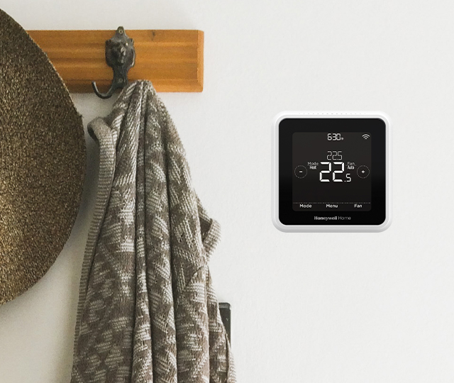 Digital thermostat on a beige wall next to a coat hanger