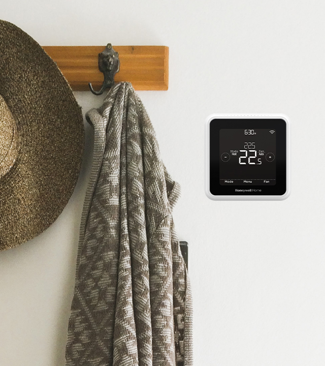 Digital thermostat on a beige wall next to a coat hanger