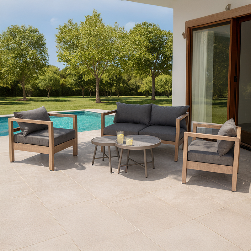 Patio furniture set with a sofa, two armchairs, and coffee tables, set on a modern poolside terrace.