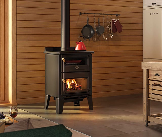 Cuisinière au bois noire avec bouilloire rouge dans un intérieur de chalet en bois.