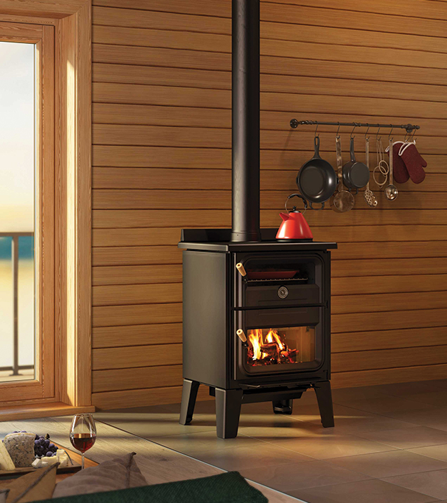 Black wood-burning stove with red kettle in a wooden cabin interior.