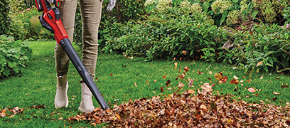 Personne utilisant un souffleur à feuilles pour ramasser les feuilles mortes sur une pelouse en automne.