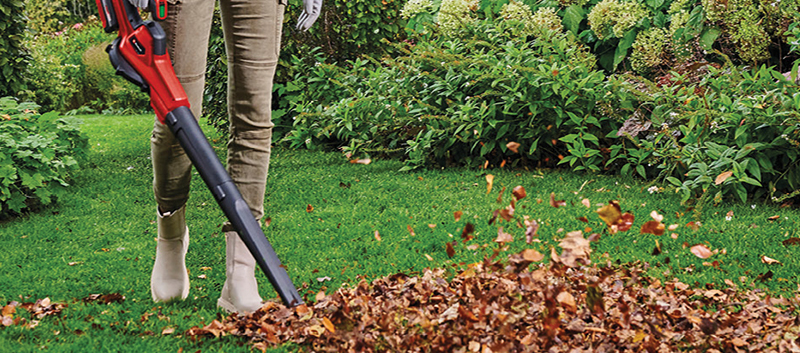 Personne utilisant un souffleur à feuilles pour ramasser les feuilles mortes sur une pelouse en automne.