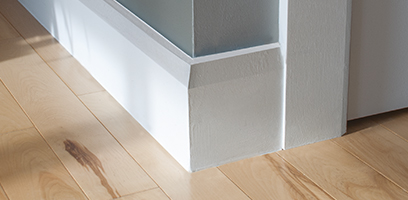 Plinthe blanche moderne install&eacute;e au bas d&rsquo;un mur, avec moulure de finition autour d&rsquo;un cadre de porte, sur un plancher de bois clair.