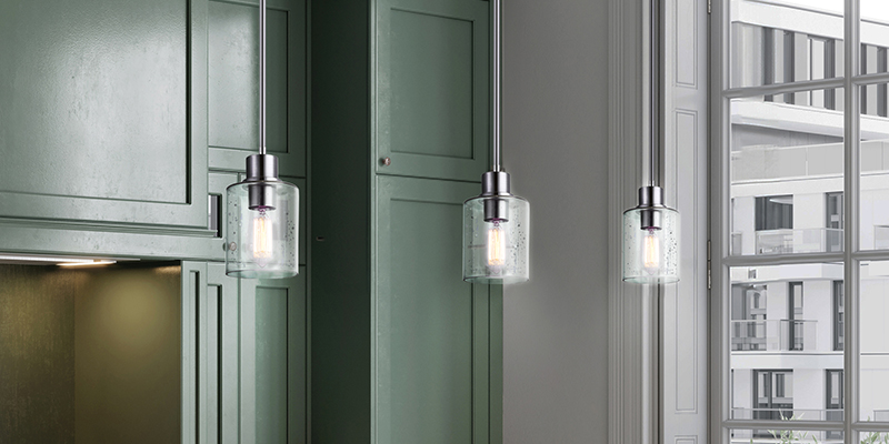 Gros plan sur un luminaire suspendu à 3 globes de verre transparent dans une cuisine aux armoires vert foncé.