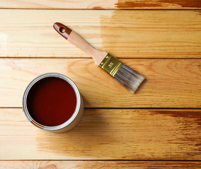 Application de teinture protectrice sur garde-corps de terrasse en bois avec pinceau, couche en cours de séchage