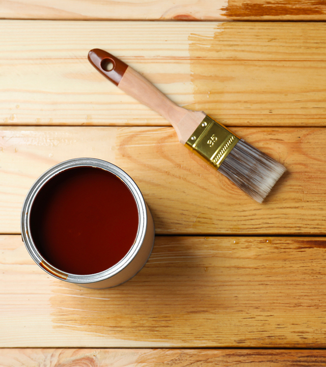 Application de teinture protectrice sur garde-corps de terrasse en bois avec pinceau, couche en cours de séchage
